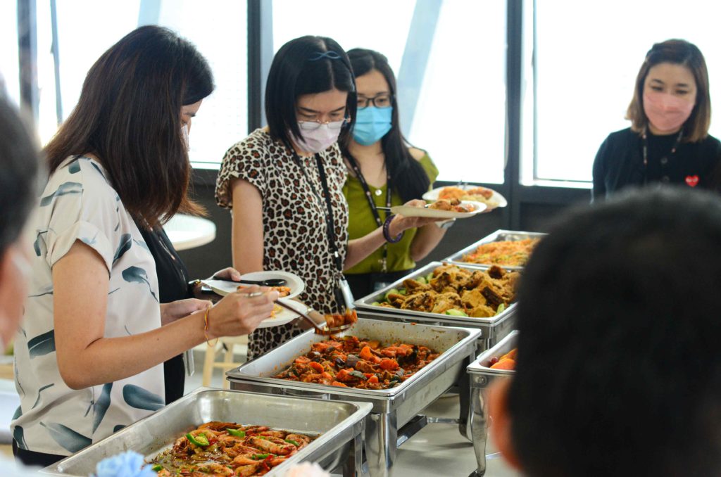 Guests wearing masks and getting food from silver trays at the office buffet catering by idocatering during 2022 COVID-19 pandemic
