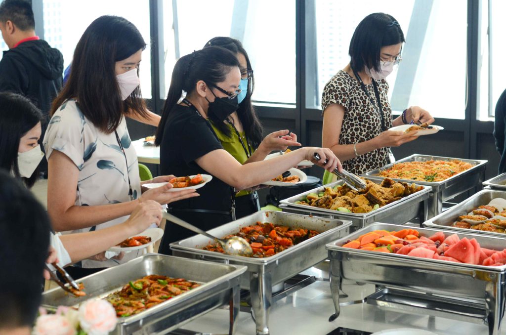 Guests wearing masks and getting food from silver trays at the office buffet catering by idocatering during 2022 COVID-19 pandemic 2